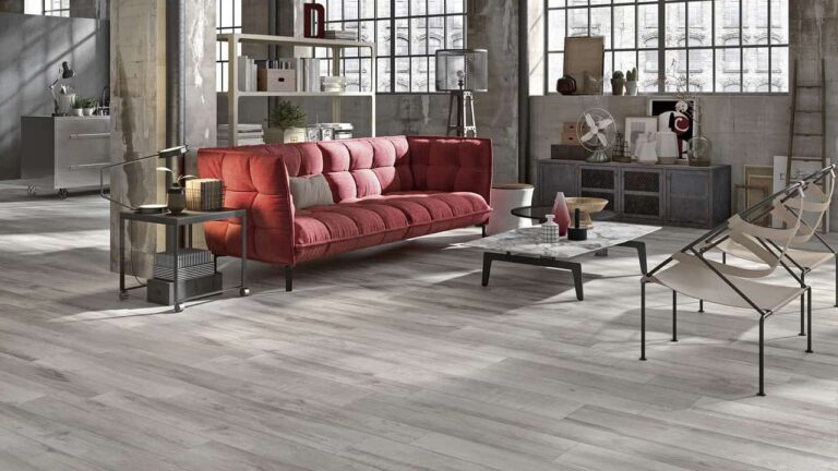 Salon loft industriel avec canapé rouge vif, carrelage effet bois gris, et décoration moderne.